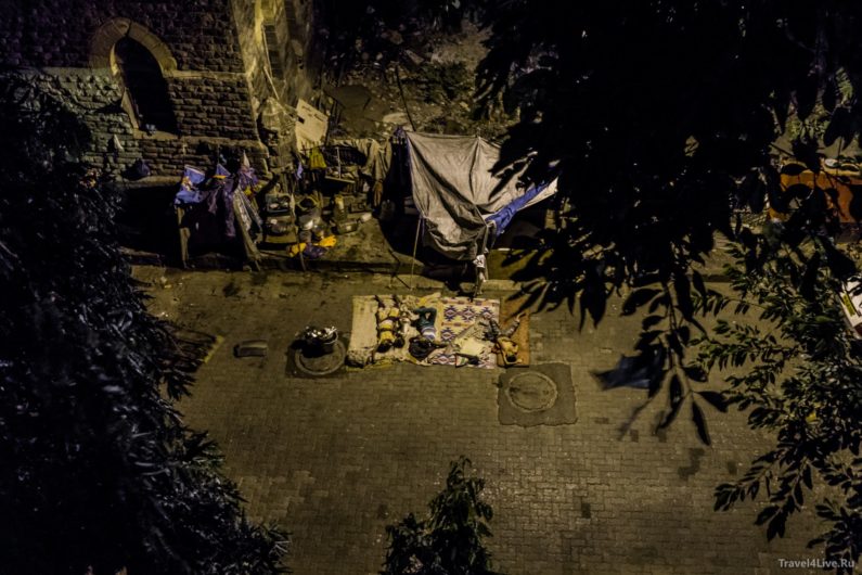 Люди спят на коврике во дворе у стены с палаткой, вид сверху ночью, Мумбаи