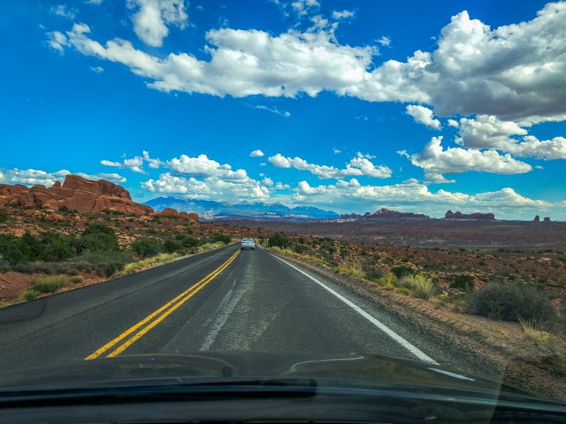 Дорога Arches Scenic Drive среди красных скал и облаков, вид из машины