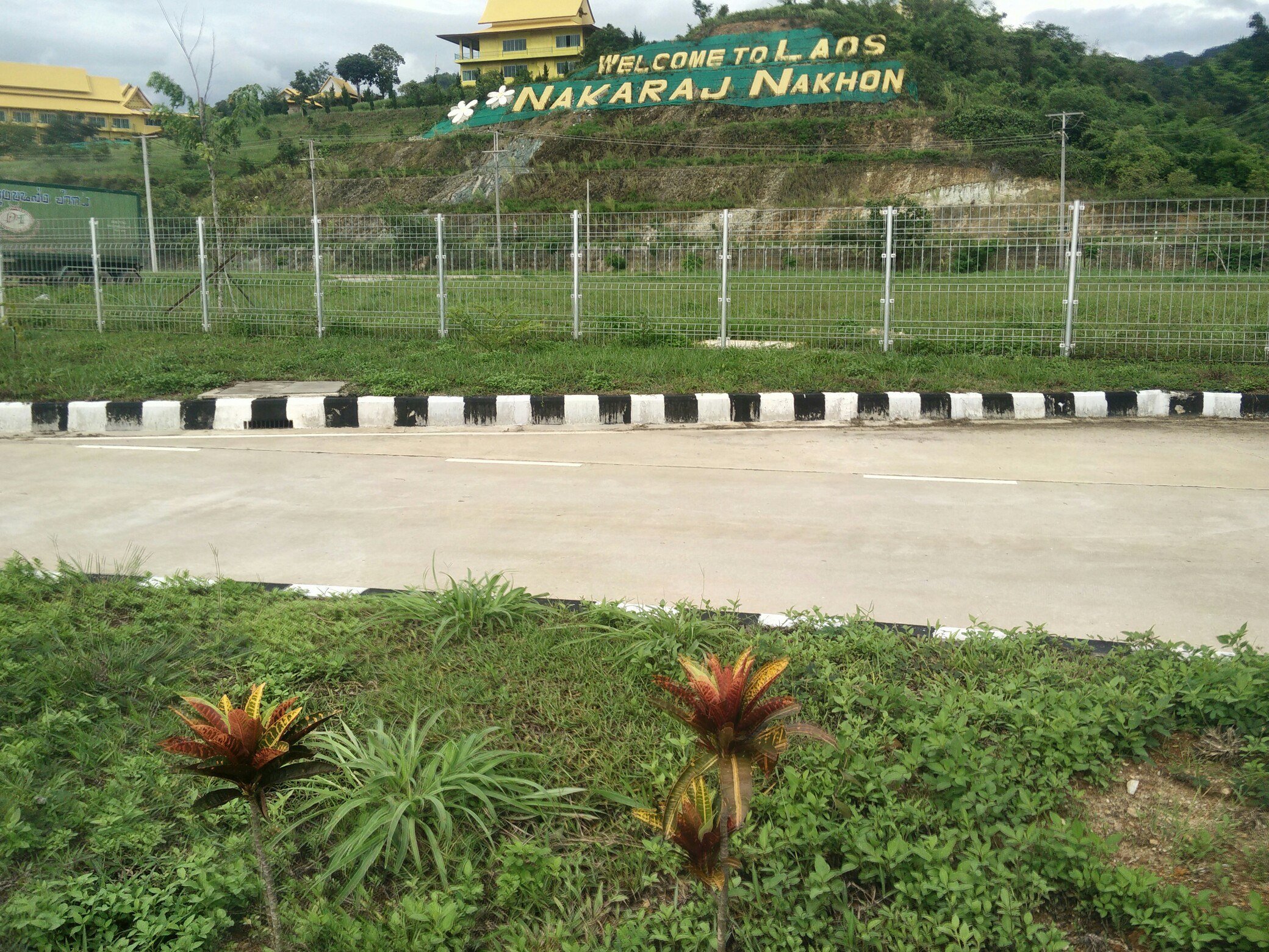 Надпись Welcome to Laos на зелёном склоне за пустой бетонной дорогой